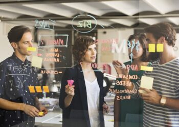 Business people discussing over plan on glass wall in office