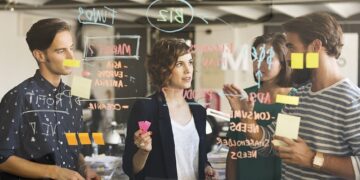 Business people discussing over plan on glass wall in office